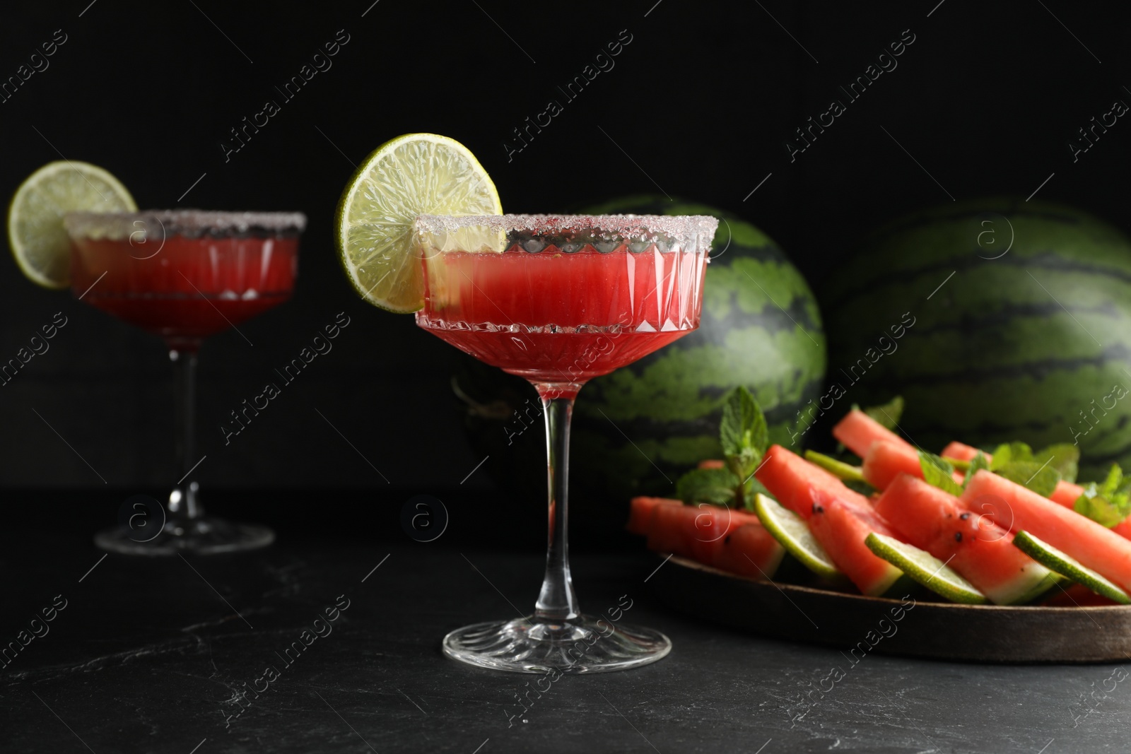 Photo of Cocktail glasses of delicious fresh watermelon juice with lime and sugar rim on black table