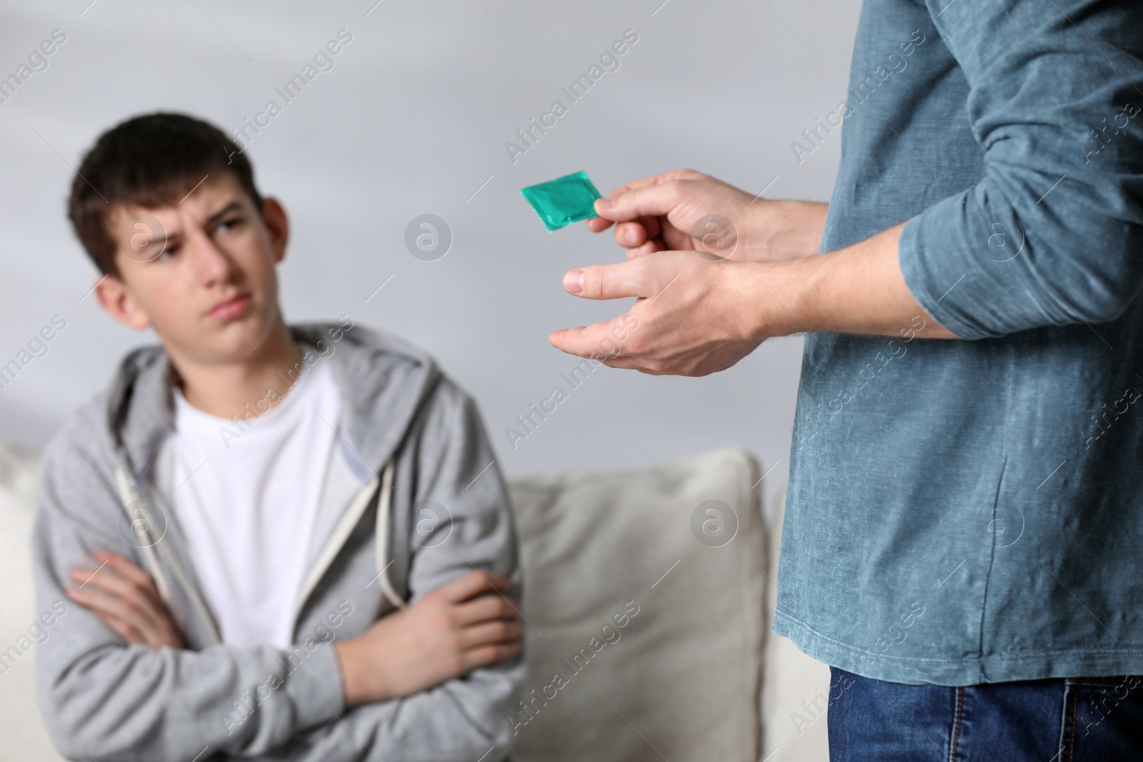 Photo of Father talking with his teenage son about contraception at home, closeup. Sex education concept