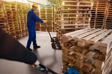 Image of Workers moving wooden pallets with manual forklift in warehouse