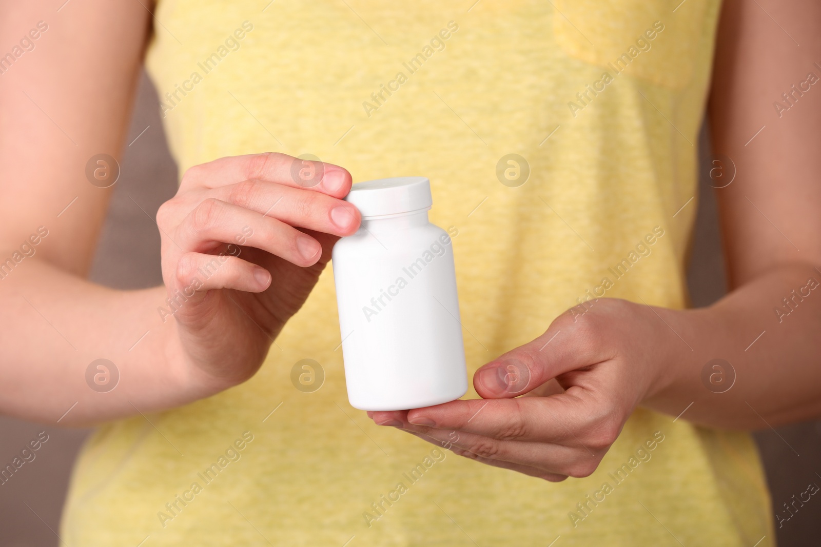 Photo of Woman holding blank white bottle with vitamin pills against light brown background, closeup