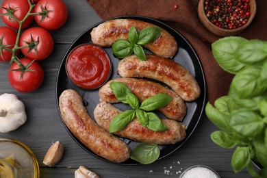 Tasty homemade sausages served with ketchup and products on grey wooden table, flat lay