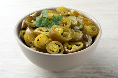 Photo of Bowl with slices of pickled green jalapeno peppers on white wooden table