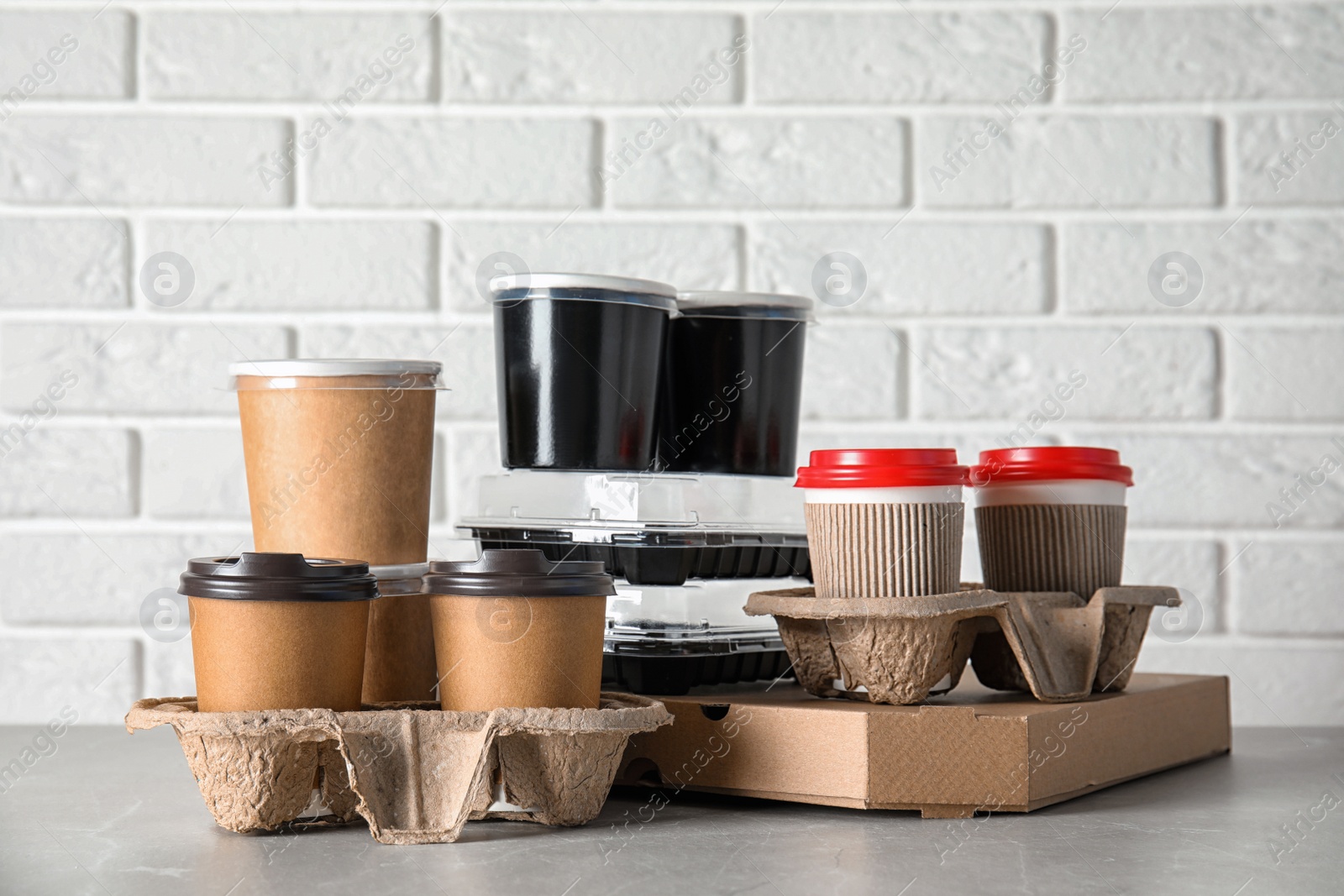 Photo of Various takeout containers on table against white brick wall. Food delivery service
