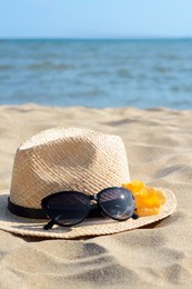 Photo of Hat with beautiful sunglasses and flowers on sand near sea. Space for text