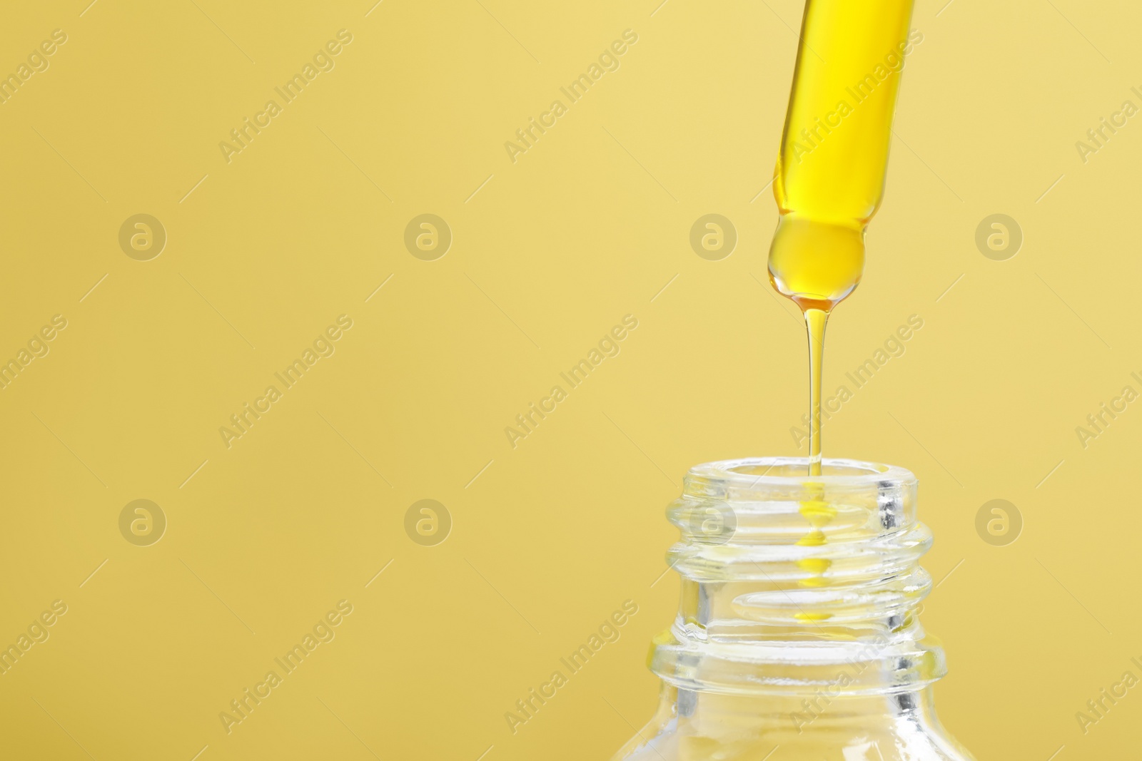 Photo of Dripping serum from pipette into bottle on yellow background, closeup. Space for text