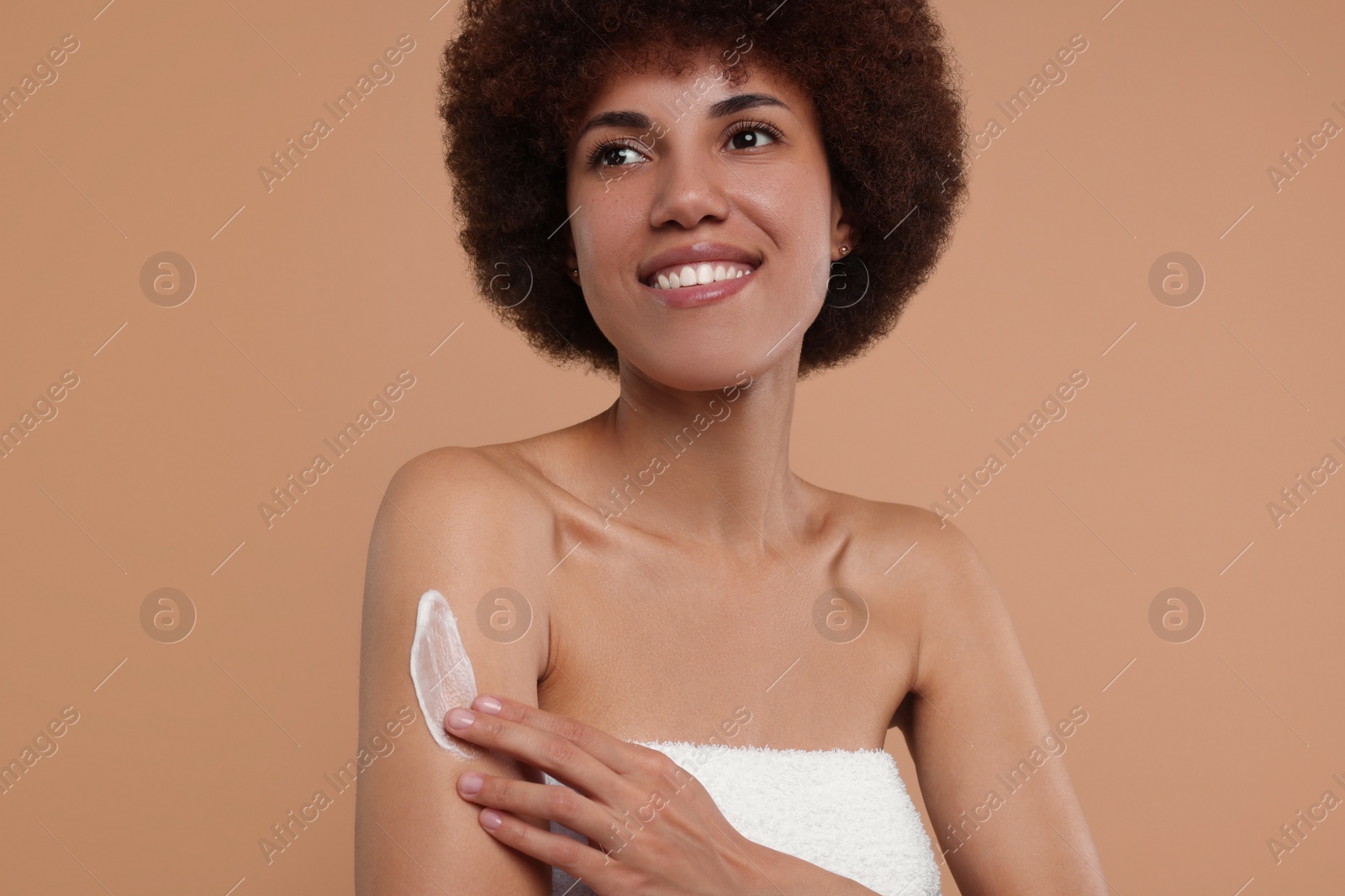 Photo of Beautiful young woman applying body cream onto arm on beige background