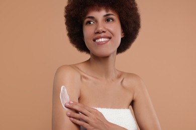 Beautiful young woman applying body cream onto arm on beige background