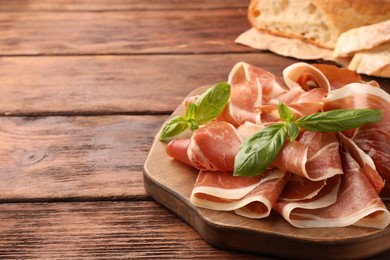 Photo of Slices of tasty cured ham and basil on wooden table, closeup. Space for text