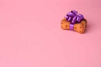 Bone shaped dog cookies with purple bow on pink background. Space for text