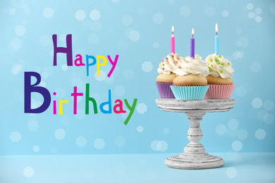 Text Happy Birthday and delicious cupcakes with candles on light blue background