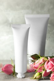 Photo of Tubes of hand cream and beautiful roses on light grey table