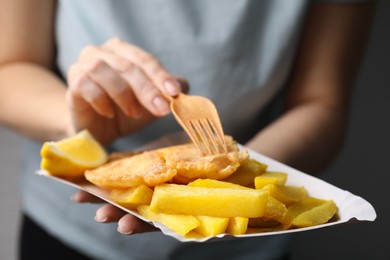 Woman eating delicious fish and chips on gray background, closeup