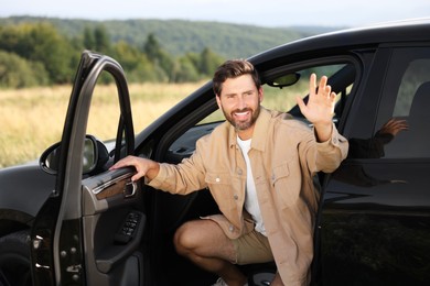 Photo of Enjoying trip. Happy bearded man waving in car