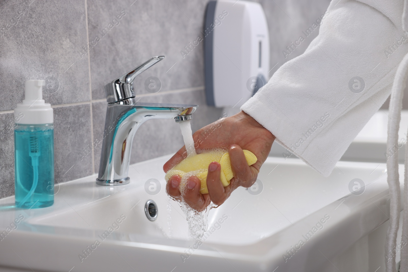 Photo of Young man cleaning face sponge above sink in bathroom, closeup