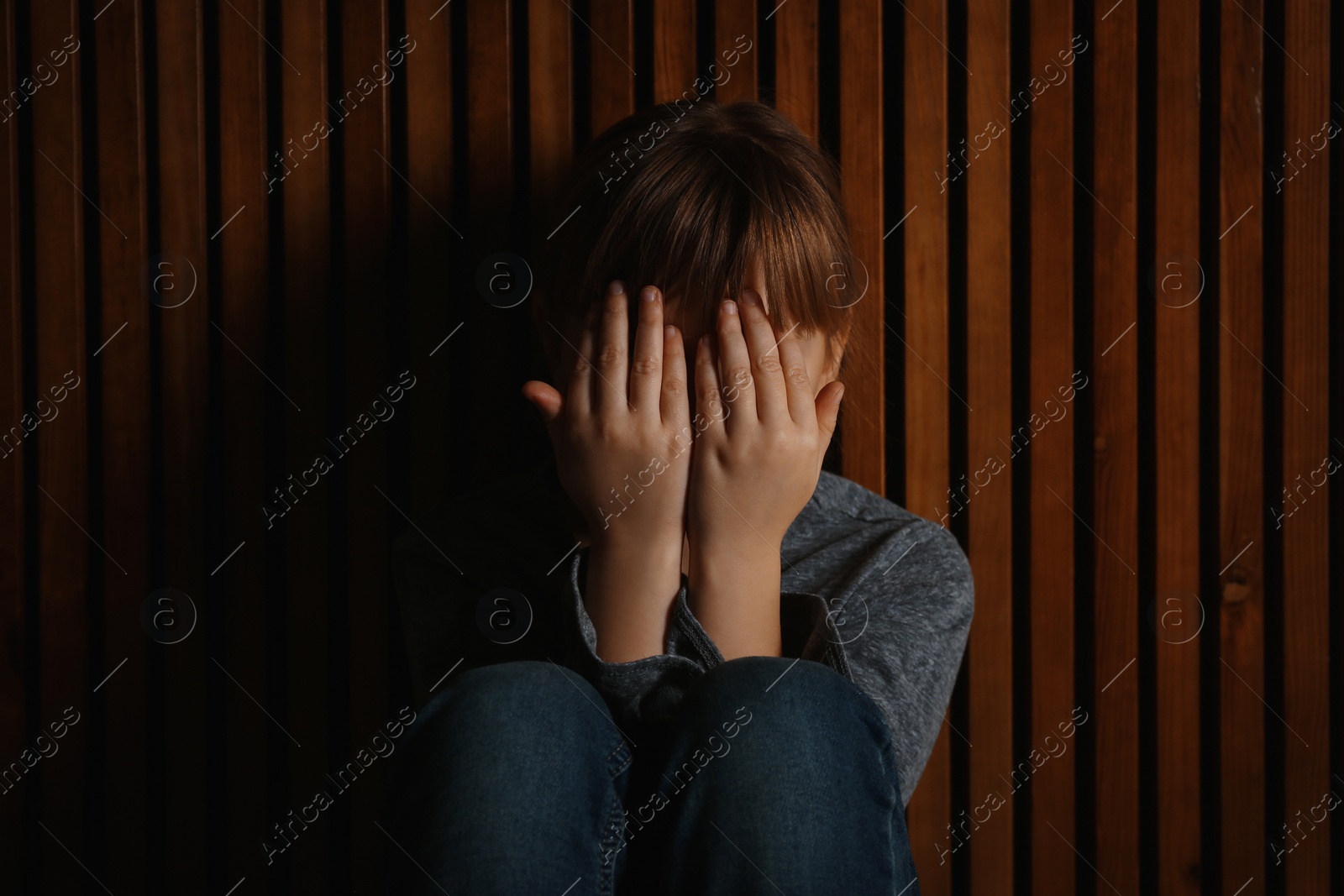 Photo of Little girl closing her eyes on wooden background. Child in danger