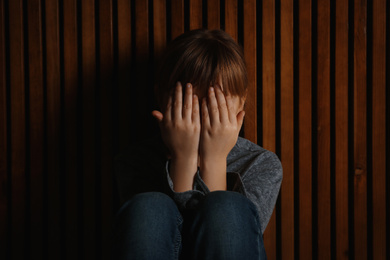 Photo of Little girl closing her eyes on wooden background. Child in danger