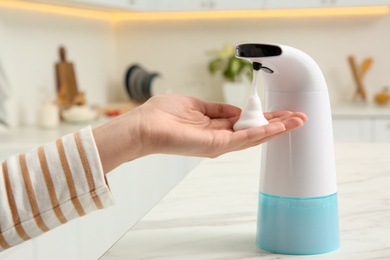 Photo of Woman using automatic soap dispenser in kitchen, closeup