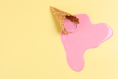 Photo of Melted ice cream and wafer cone on pale yellow background, top view. Space for text
