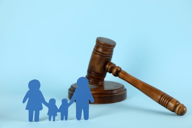Photo of Paper family figure and wooden gavel on light blue background. Child adoption concept