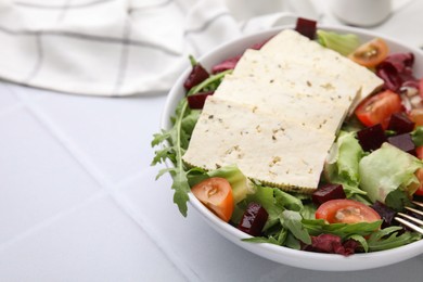 Bowl of tasty salad with tofu and vegetables on white tiled table, closeup. Space for text