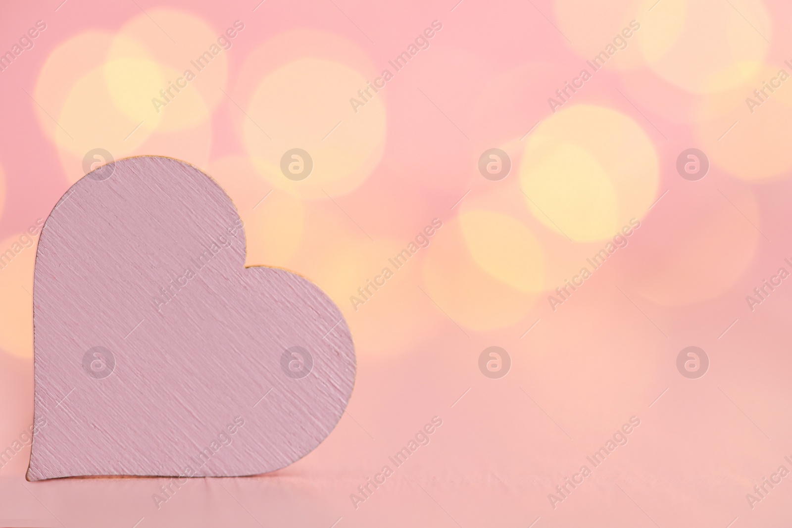 Photo of White heart on wooden table against festive lights, space for text. St. Valentine's day