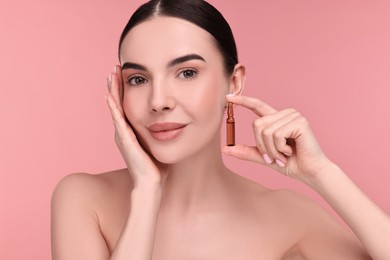 Beautiful young woman holding skincare ampoule on pink background