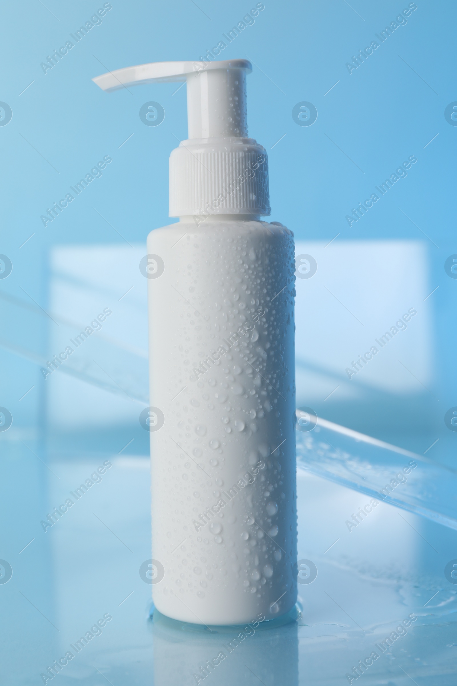 Photo of Wet bottle of face cleansing product on light blue background