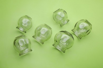 Glass cups on light green background, flat lay. Cupping therapy