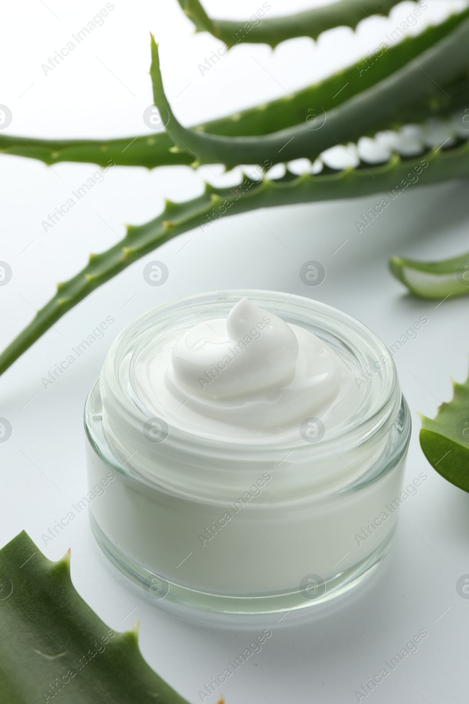 Photo of Jar of natural cream and aloe leaves on white background, closeup