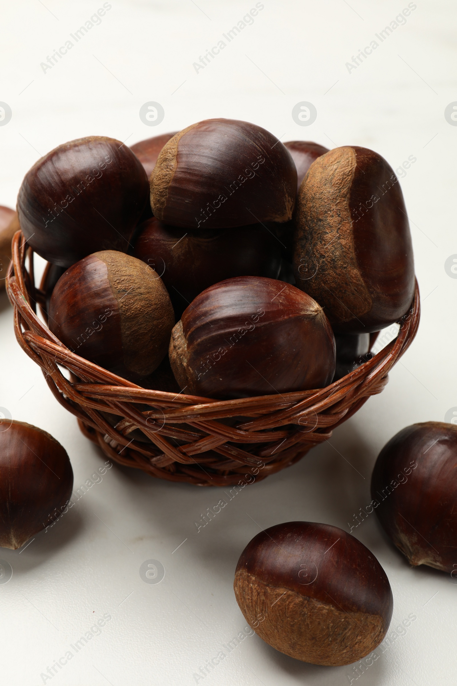 Photo of Sweet fresh edible chestnuts in wicker bowl on white table, closeup