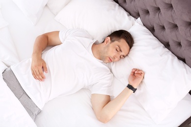 Young man sleeping in bed at home, top view