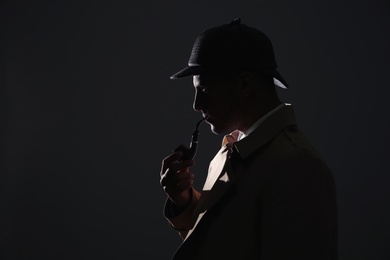 Photo of Old fashioned detective with smoking pipe on dark background. Space for text
