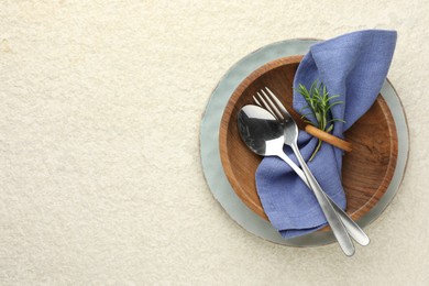 Photo of Stylish setting with cutlery, napkin, rosemary and plates on light textured table, top view. Space for text