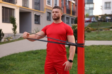 Muscular man doing exercise with elastic resistance band outdoors