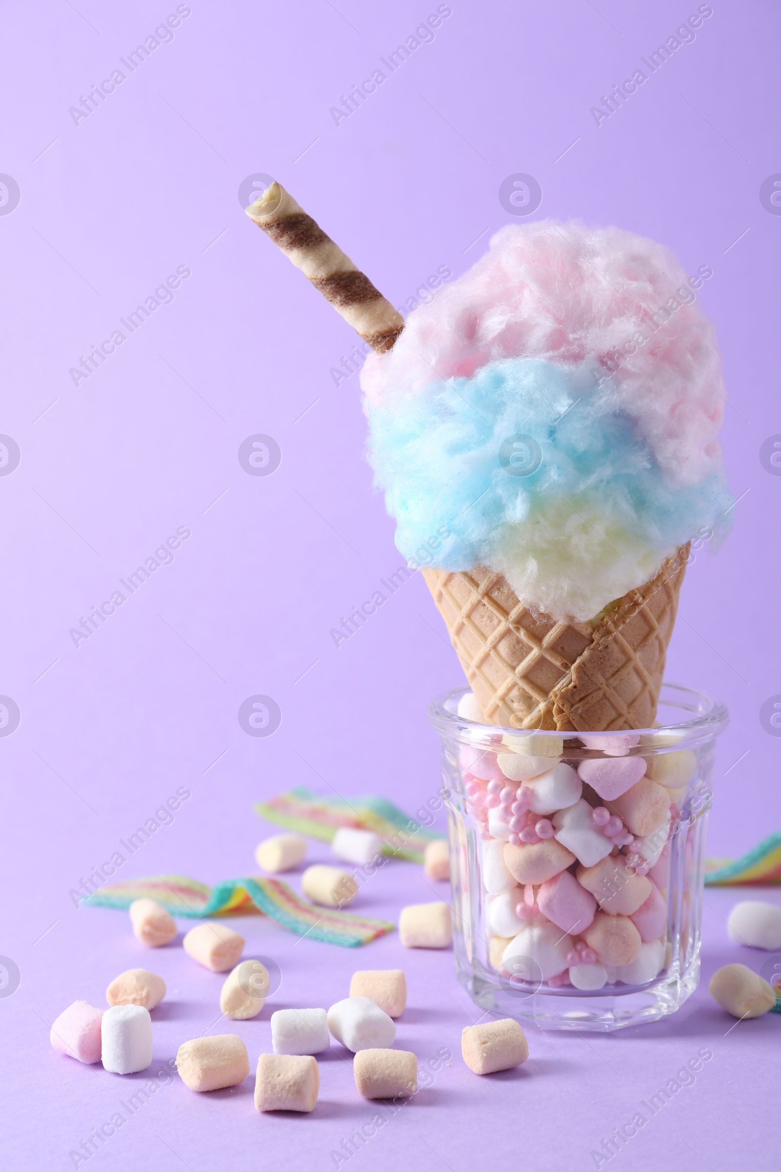 Photo of Sweet cotton candy in waffle cone and marshmallows on purple background