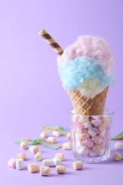 Photo of Sweet cotton candy in waffle cone and marshmallows on purple background