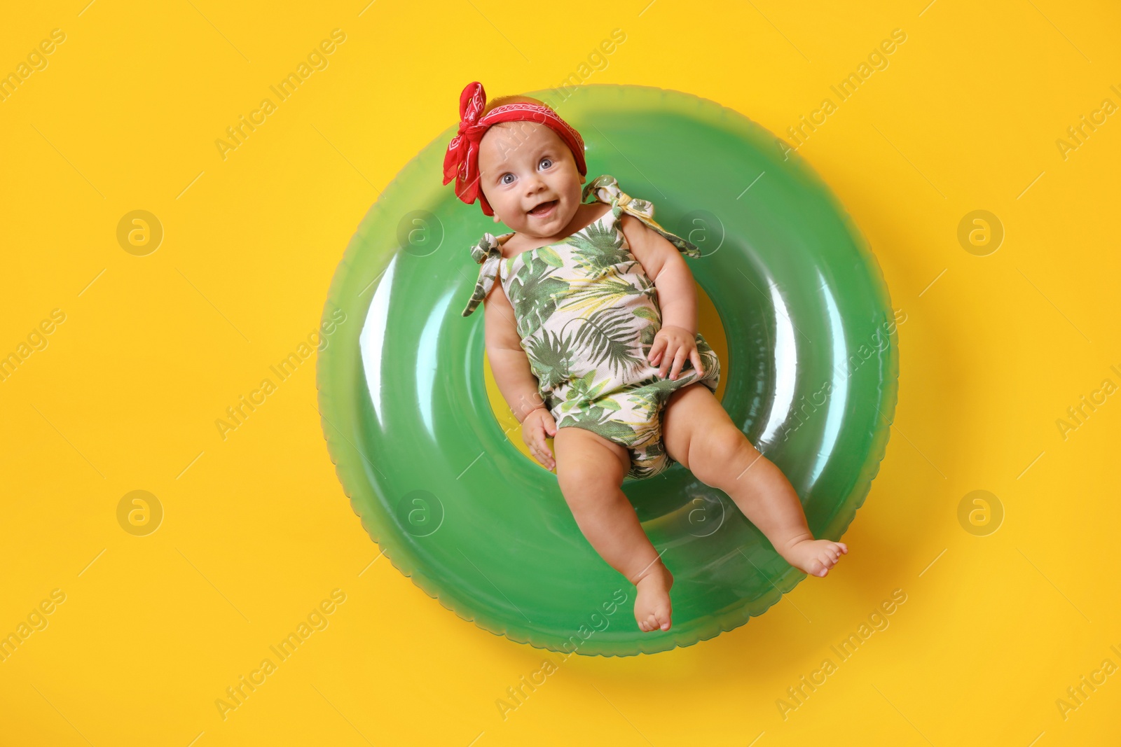 Photo of Cute little baby in headband with inflatable ring on yellow background