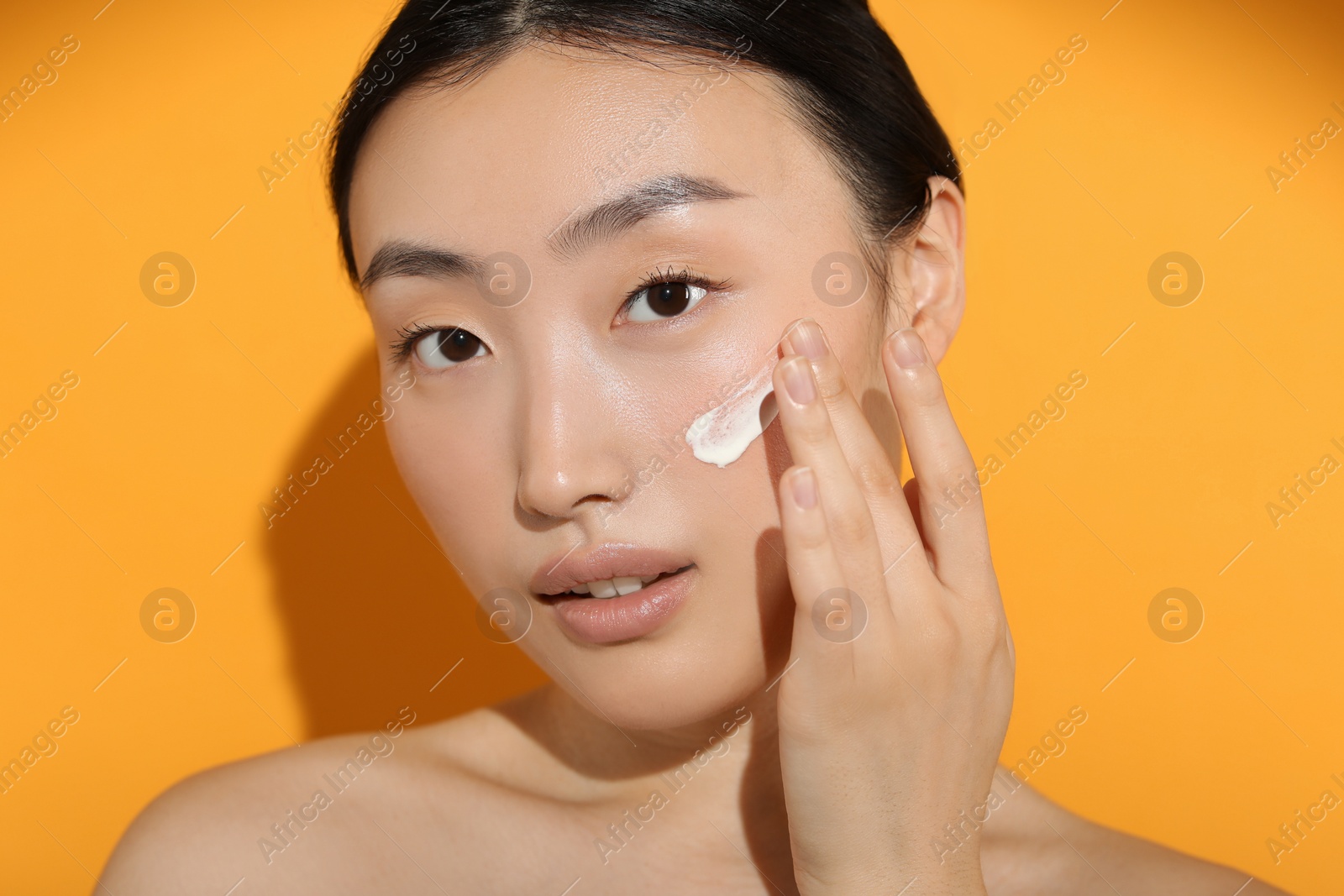 Photo of Beautiful young woman in sunlight with sun protection cream on her face against orange background