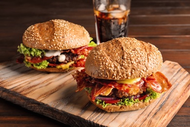 Photo of Tasty burgers with bacon on wooden board