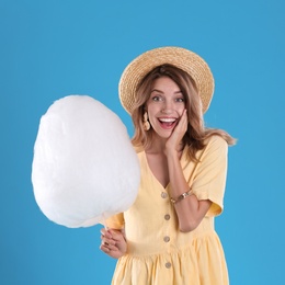 Photo of Emotional young woman with cotton candy on blue background