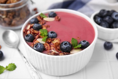 Photo of Bowl of delicious smoothie,served with fresh blueberries and granola on white tiled table, closeup