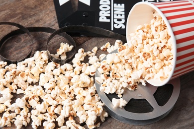 Tasty popcorn, film reel and clapperboard on wooden table. Cinema snack