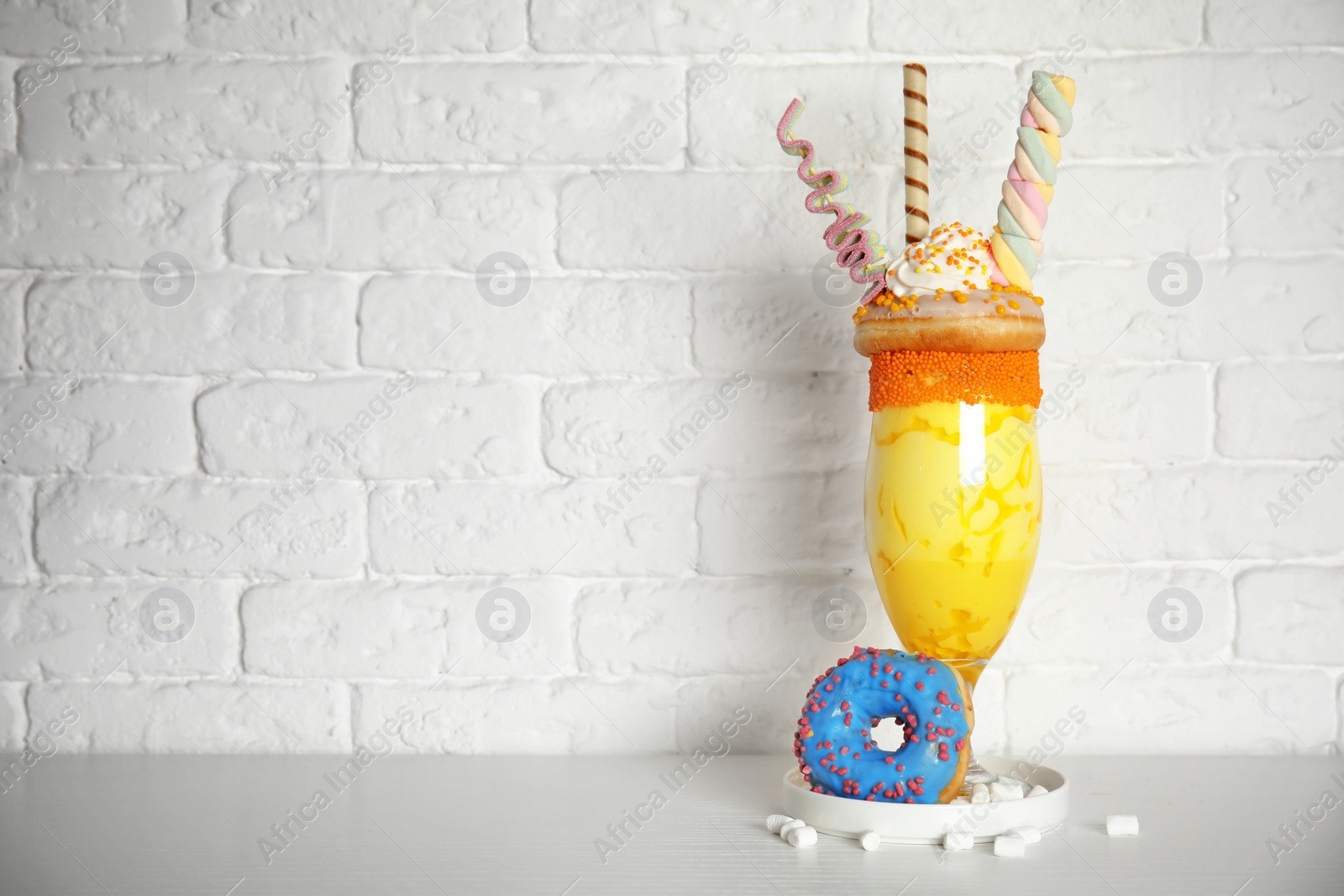 Photo of Glass of tasty milk shake with sweets on table near brick wall. Space for text
