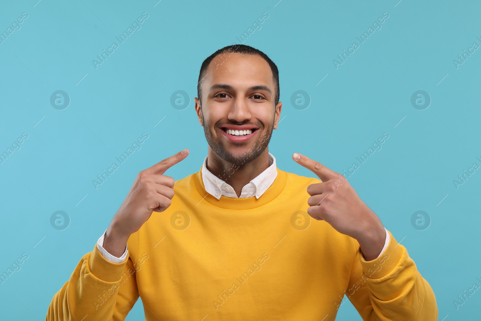 Photo of Smiling man pointing at his healthy clean teeth on light blue background