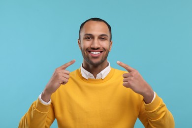 Photo of Smiling man pointing at his healthy clean teeth on light blue background