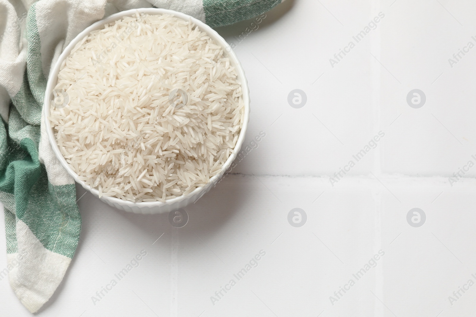 Photo of Raw basmati rice in bowl on white tiled table, top view. Space for text