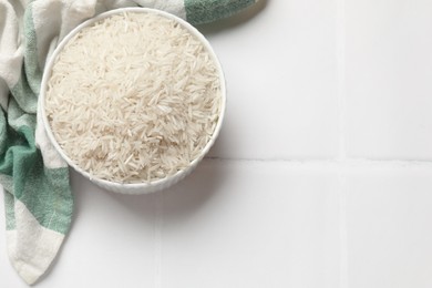 Photo of Raw basmati rice in bowl on white tiled table, top view. Space for text