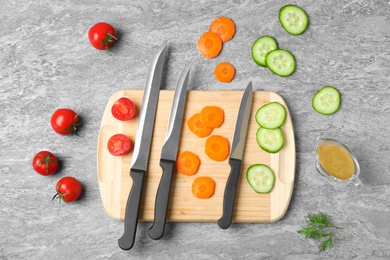 Photo of Flat lay composition with cutting board, knives and vegetables on grey background