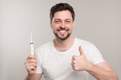 Happy man holding electric toothbrush on light grey background