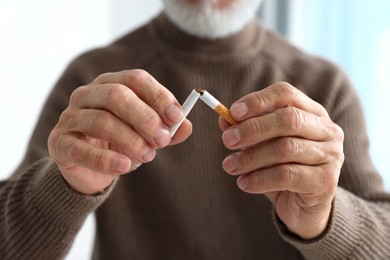 Stop smoking concept. Man breaking cigarette on light background, closeup